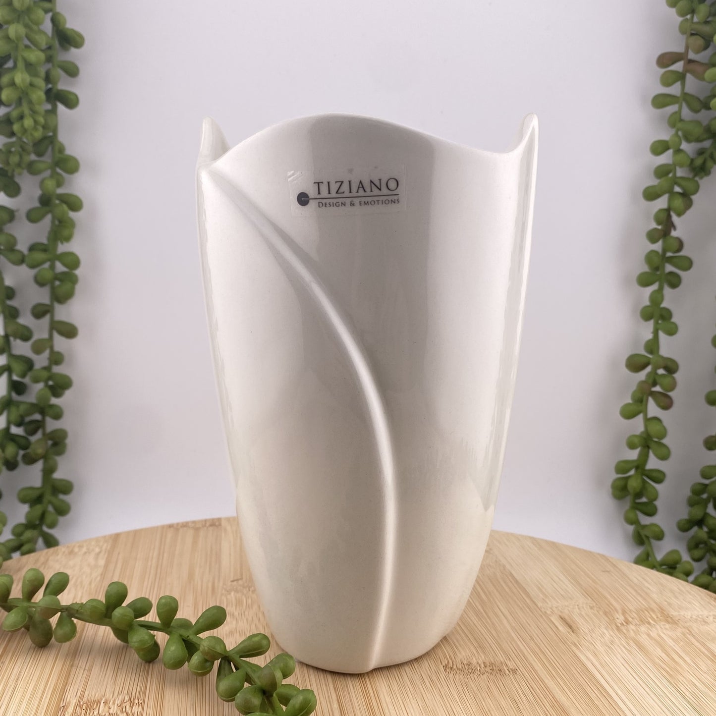 Eine Blumenvase aus creme-weißer Keramik im schlichten Design ist im Ambiente platziert.