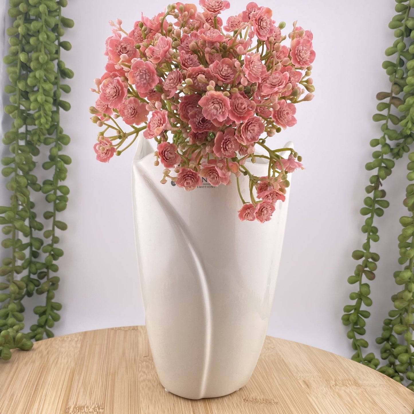 Eine Blumenvase aus creme-weißer Keramik im schlichten Design mit rosanen Blumen. Die Vase ist im Ambiente platziert.