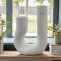 Keramik geschwungene U-Vase steht auf einer Fensterbank und ist von Pflanzen umgeben; ihre glänzende weiße Keramik wirkt modern und elegant im natürlichen Tageslicht.
