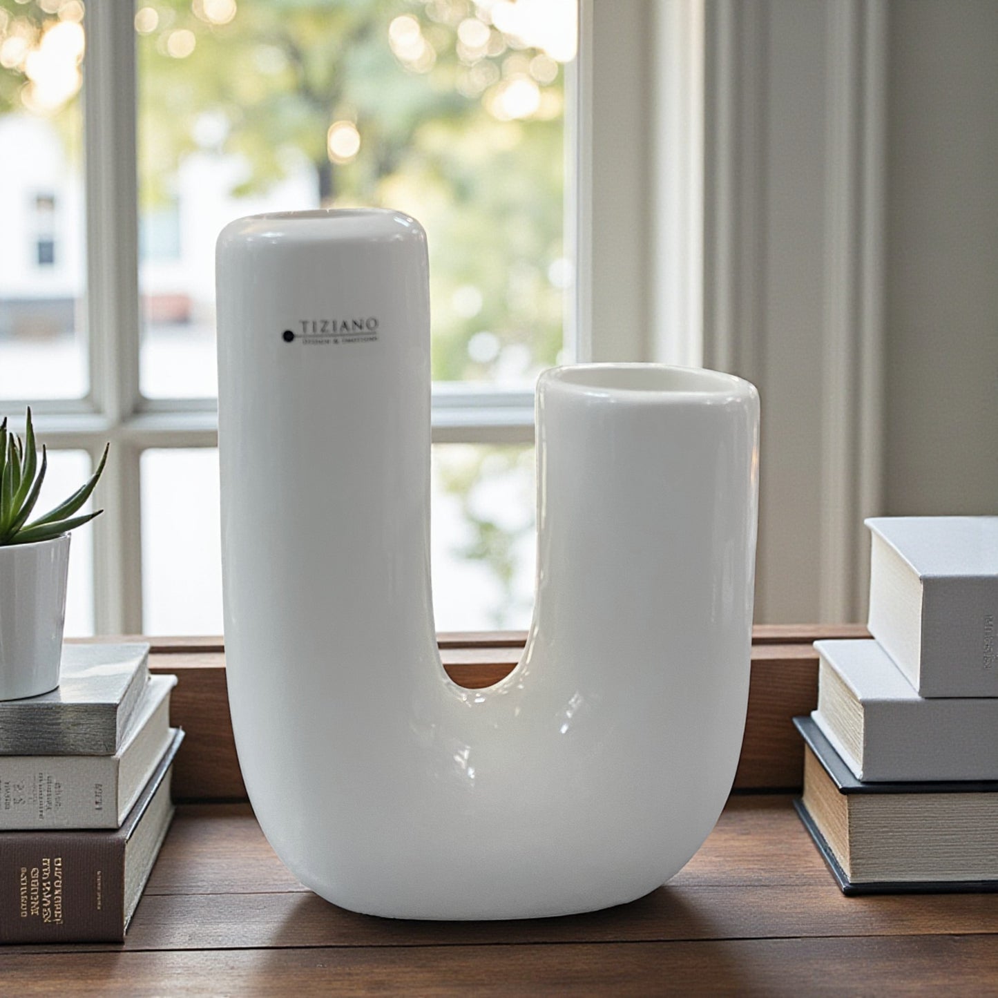 Keramik U-Vase steht auf einem Holztisch vor einem Fenster und ist von Büchern und einer kleinen Pflanze dekorativ eingerahmt; die glatte Oberfläche betont das minimalistische Design.