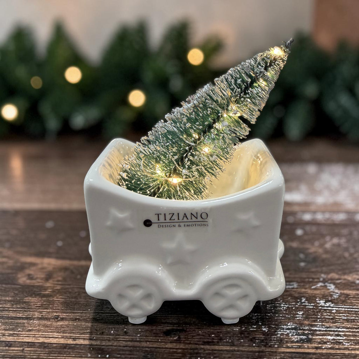 Cremeweißer Tiziano Keramik Weihnachtszug-Waggon mit beleuchtetem Weihnachtsbaum auf einem dunklen Holztisch vor Tannengrün und warmweißer Lichterkette.