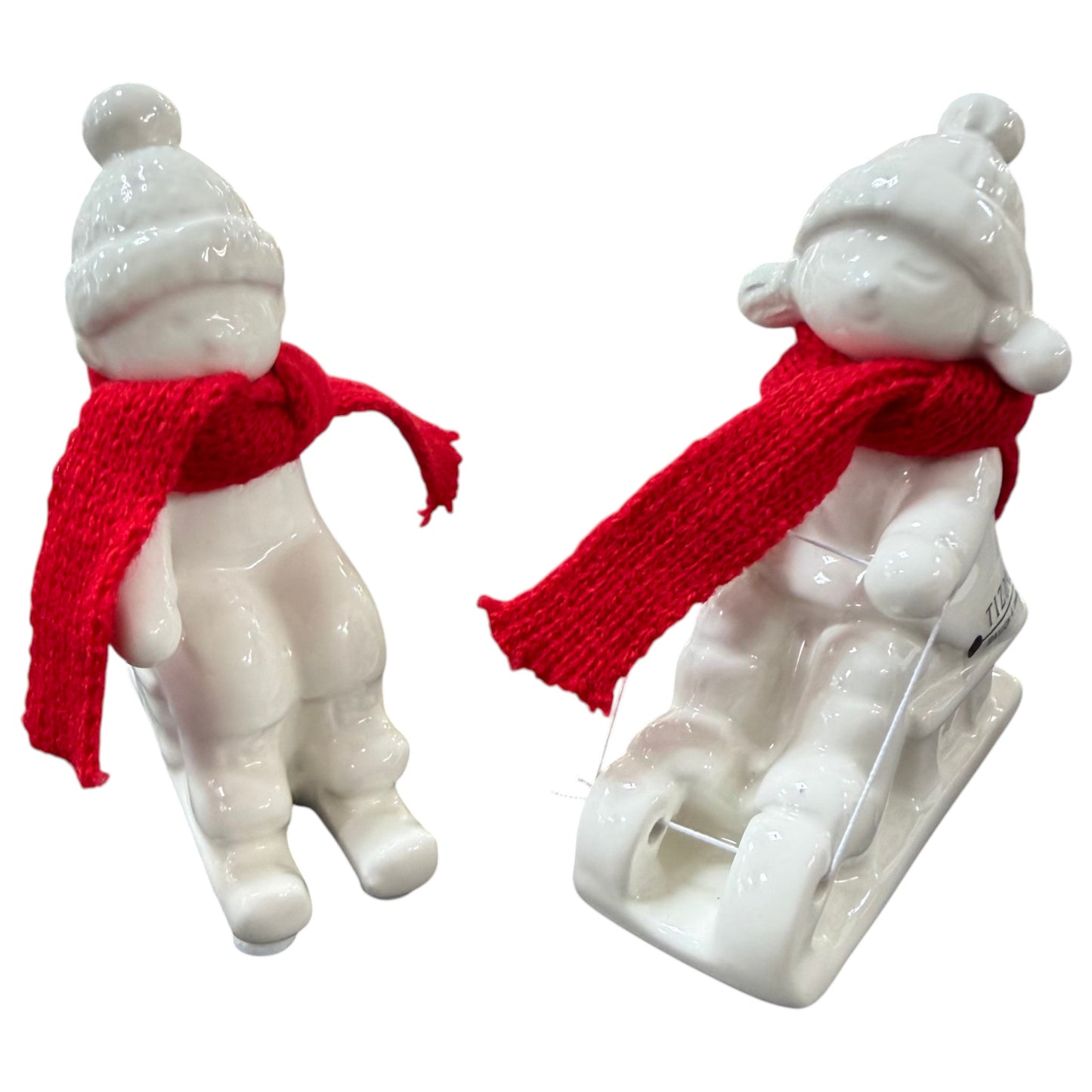 Zwei cremeweiße Tiziano Keramik-Winterkinder mit roten Schals, eines sitzend und eines auf einem Schlitten, vor weißem Hintergrund.
