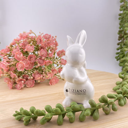 Ein kleiner Keramik Osterhase, der ein Osterei in seinen Pfoten hält und eine Schleife um den Hals gebunden hat. Die Ohren sind ausgestreckt. Der Dekohase ist aus creme-weißer Keramik gefertigt und 9cm groß.