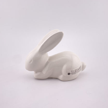 Ein kleiner schlafender Keramik Osterhase, der auf dem Boden liegt und seine Ohren ausstreckt.. Der Dekohase ist aus creme-weißer Keramik gefertigt, 10cm hoch und vor weißem Hintergrund abgebildet.