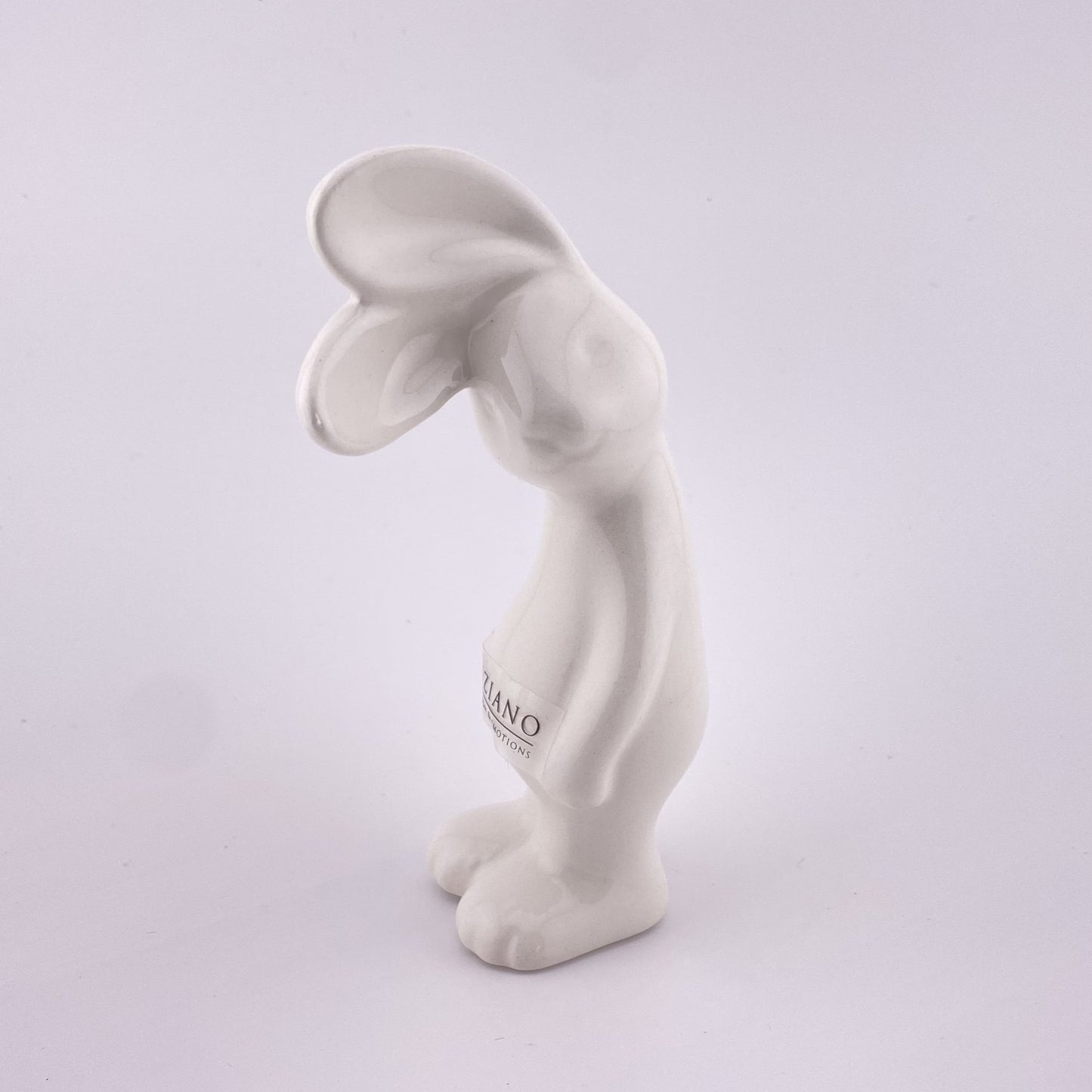 Ein kleiner creme-weißer Keramik Osterhase, der sein Gesicht zur Seite geneigt hat und mit seinen abstehenden Öhrchen lauschht. Er steht auf seinen Beinen und seine Arme hängen hinterunter. Der Deko Hase ist 13 cm hoch und vor weißem Hintergrund platziert. 