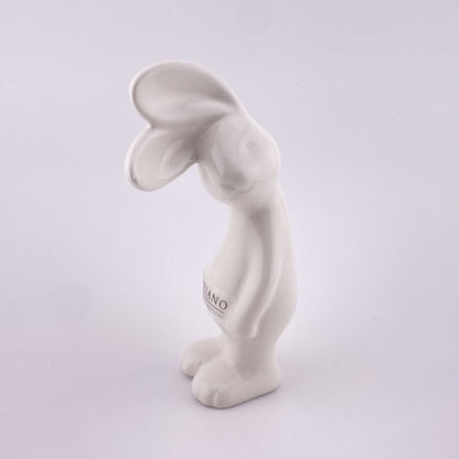 Ein kleiner creme-weißer Keramik Osterhase, der sein Gesicht zur Seite geneigt hat und mit seinen abstehenden Öhrchen lauschht. Er steht auf seinen Beinen und seine Arme hängen hinterunter. Der Deko Hase ist 13 cm hoch und vor weißem Hintergrund platziert. 