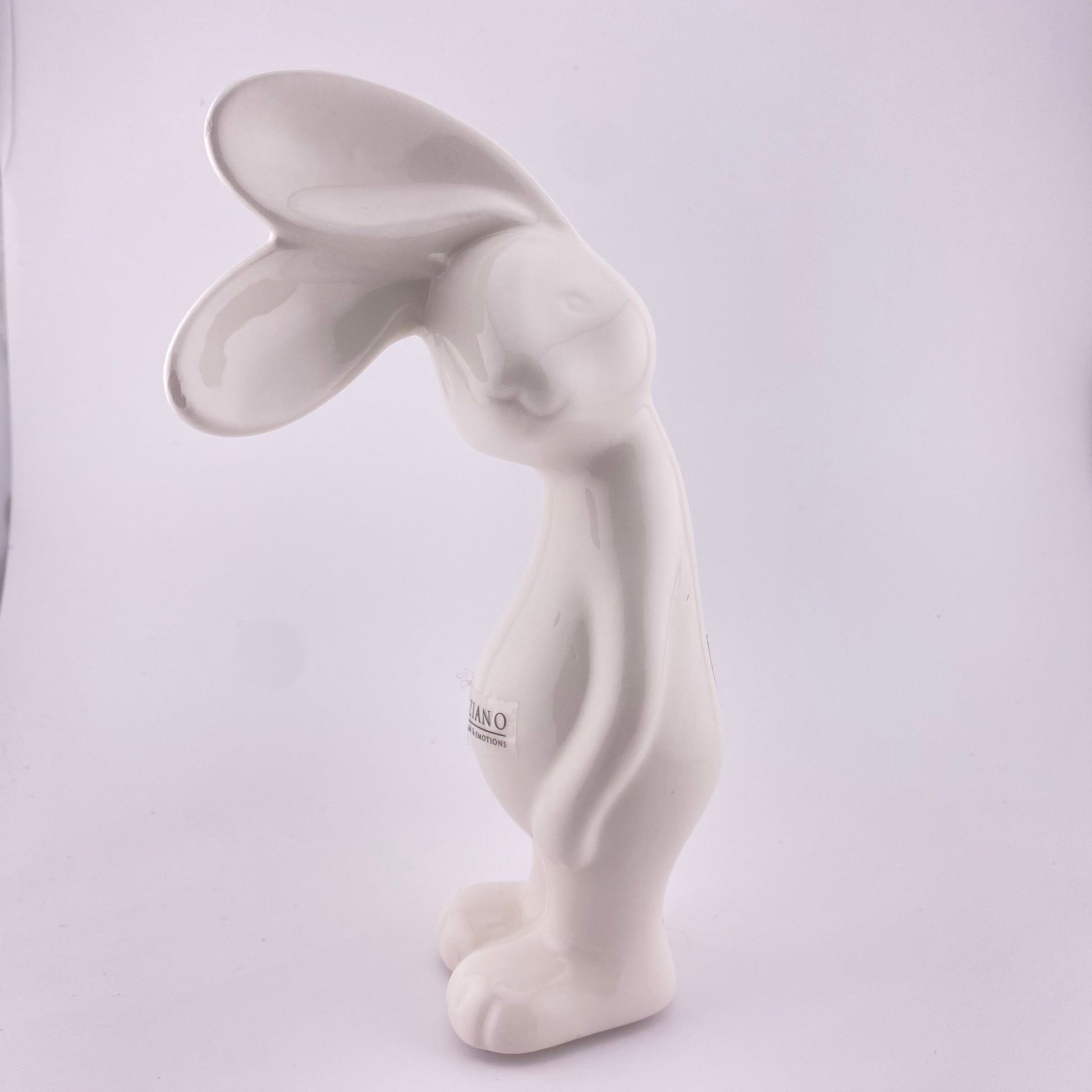 Ein creme-weißer Keramik Osterhase, der sein Gesicht zur Seite geneigt hat und mit seinen abstehenden Öhrchen lauschht. Er steht auf seinen Beinen und seine Arme hängen hinterunter. Der Deko Hase ist 18 cm hoch und vor weißem Hintergrund platziert. 