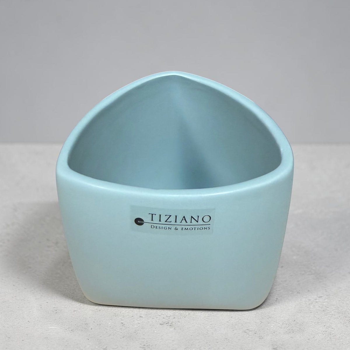 Kleines Tiziano Pflanzgefäß in Laguna Blau mit leicht geschwungener Öffnung auf grauem Untergrund.