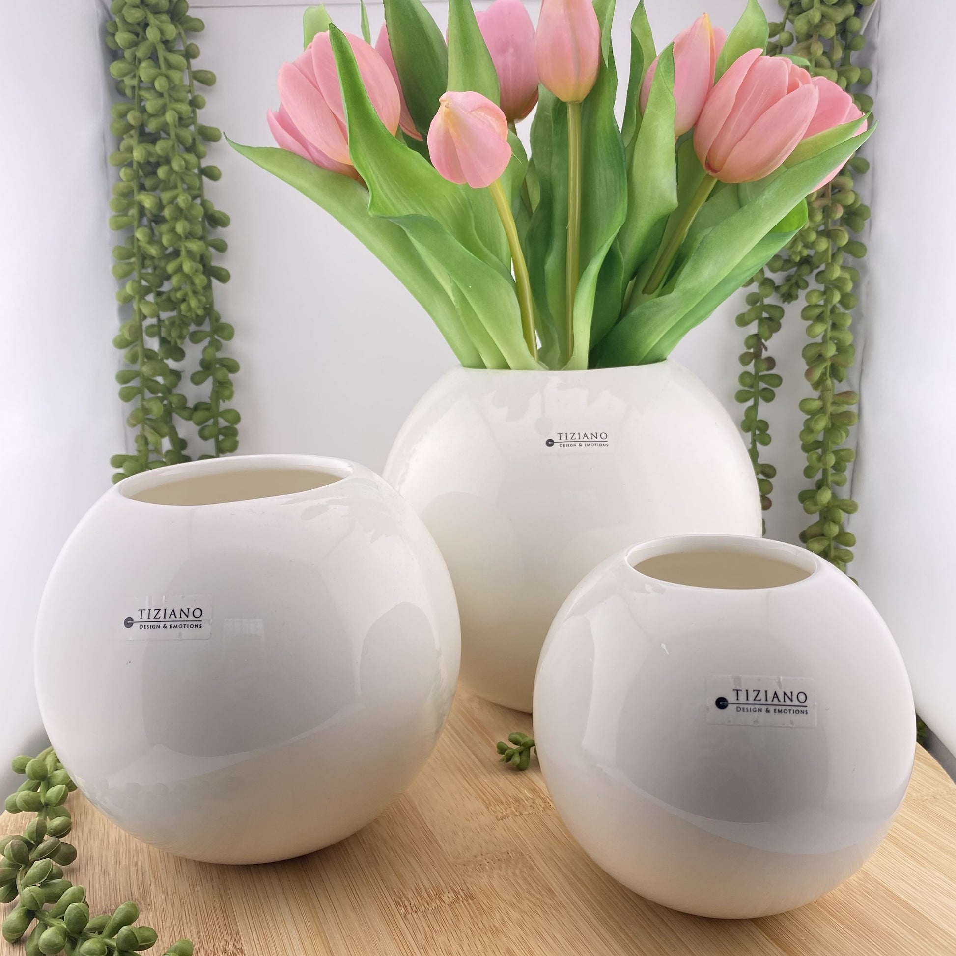 Drei runde Blumenvasen aus creme-weißer Keramik, die unterschiedlich hoch und im Ambiente mit rosanen Tulpen platziert sind. 