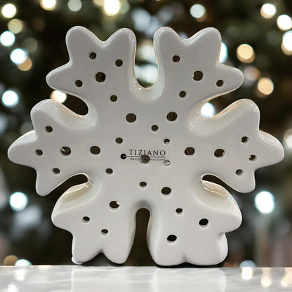 Eine weiße Schneeflocke aus Keramik mit kleinen runden Öffnungen im Ambiente. Auf der Vorderseite ist das Logo „Tiziano Design & Emotions“ zu sehen.
