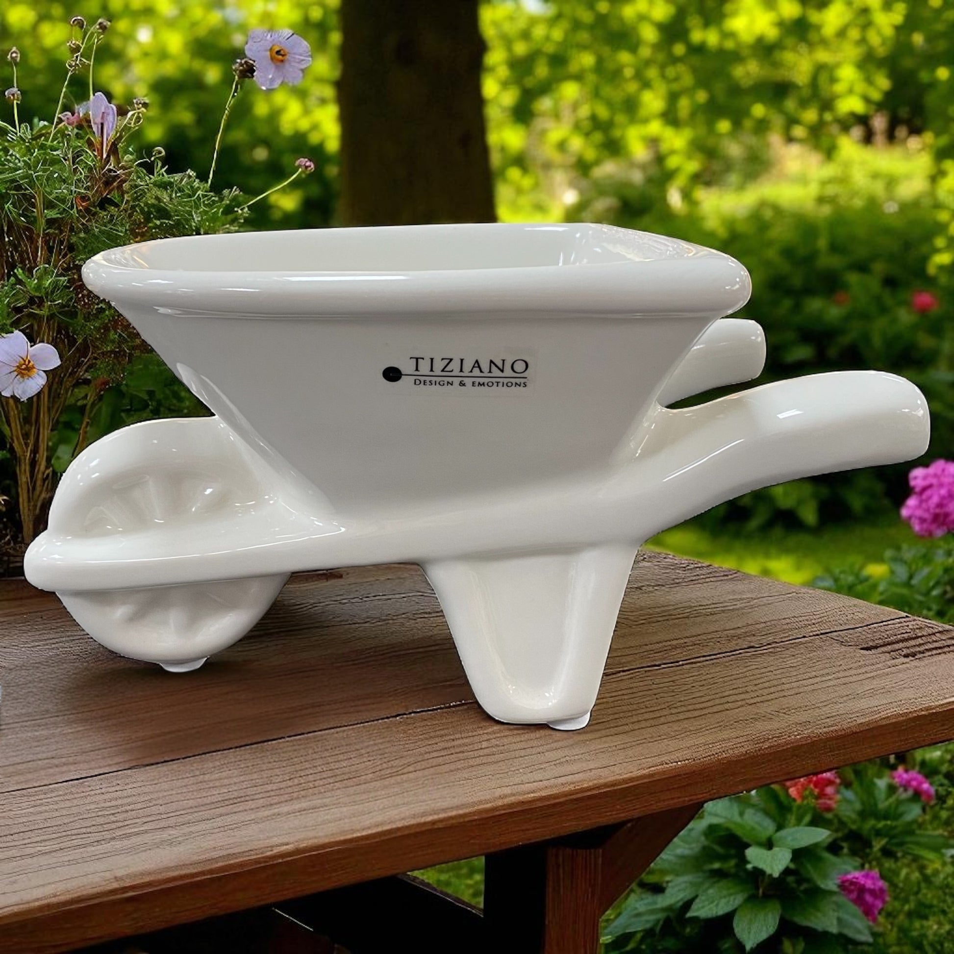 Eine Tiziano Pflanzschale in Form einer creme-weißen Keramik Schubkarre mit Rad und Griffen im Ambiente