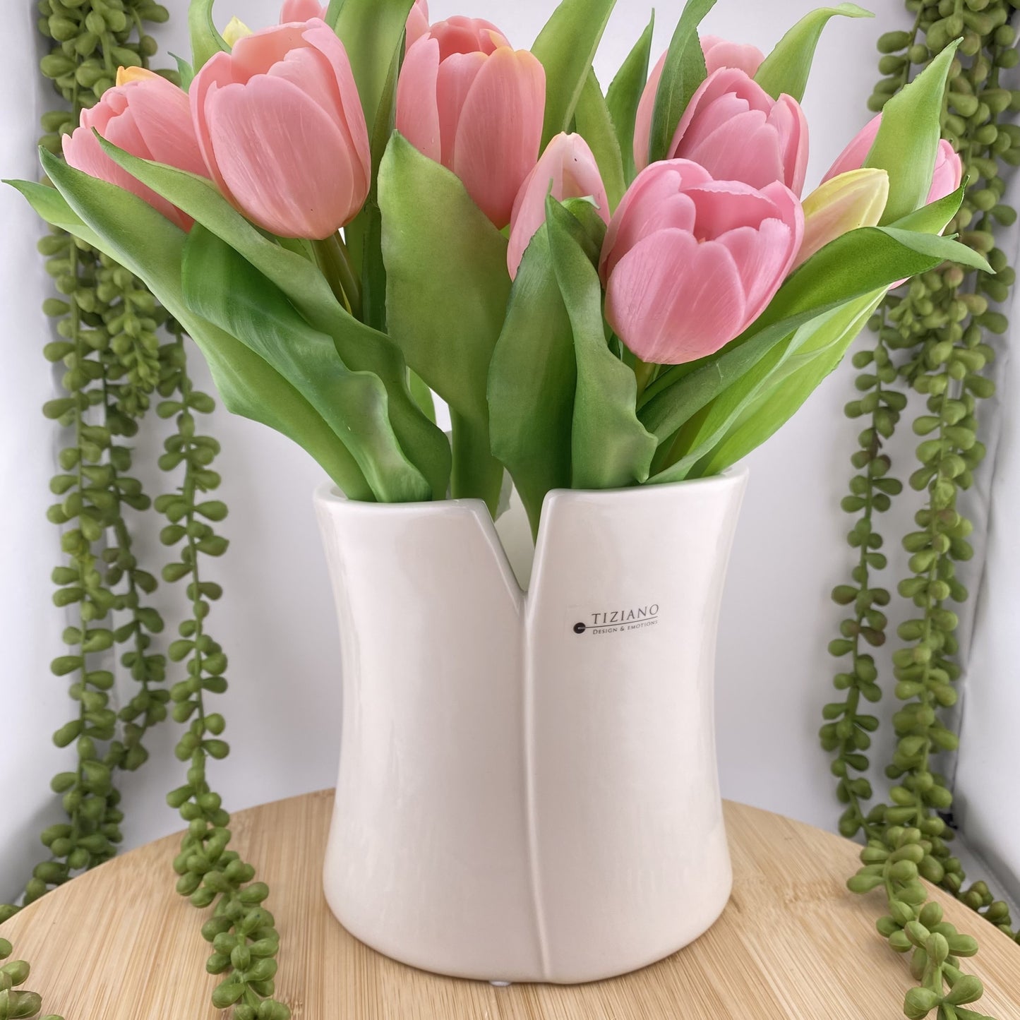 Eine zeitlose Keramikvase in creme-weißer Farbe und mit einer Höhe von 15cm  ist mit pinken Tulpen im Ambiente platziert. 