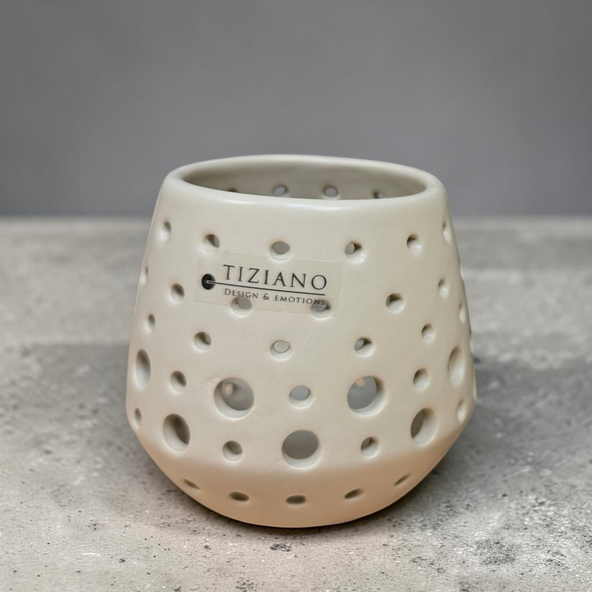 Kleines Tiziano Teelicht Rodano in Avena Beige mit unterschiedlich großen runden Aussparungen vor grauem Hintergrund.