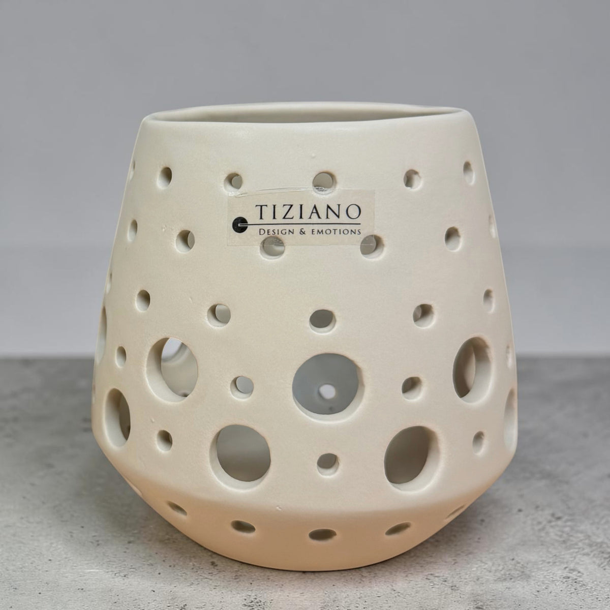 Tiziano Teelicht Rodano in Avena Beige mit unterschiedlich großen runden Aussparungen auf grauem Untergrund.