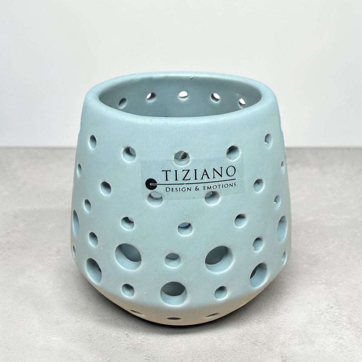 Kleines Tiziano Teelicht Rodano in Laguna Blau mit unterschiedlich großen runden Aussparungen vor grauem Hintergrund.
