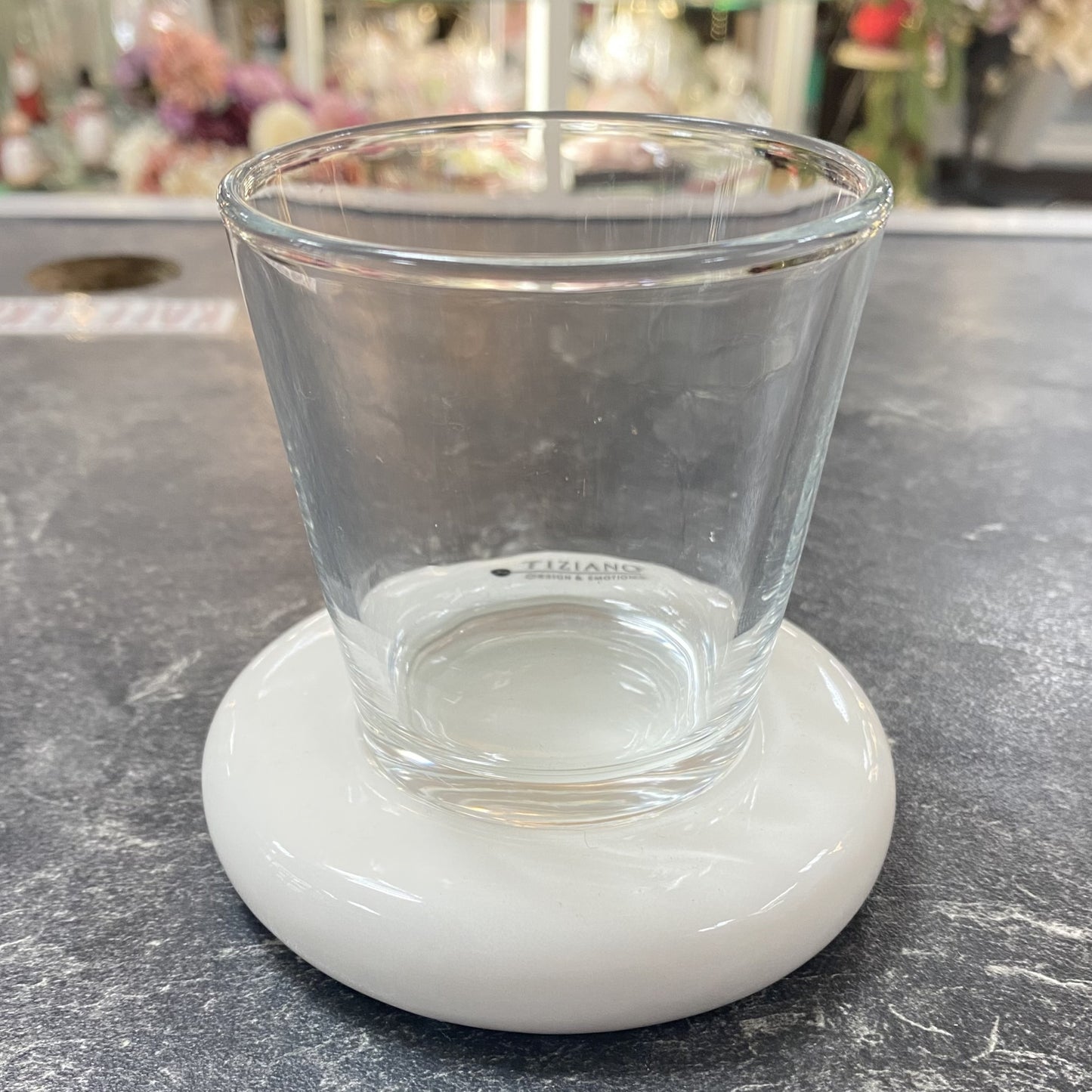 Teelichthalter aus Glas mit weißer Keramikplatte von Tiziano, dekorativ arrangiert auf dunkler Oberfläche im Wohnambiente.