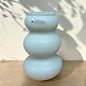 Kleine Tiziano Vase in Laguna Blau mit drei abgerundeten Formelementen auf einer Holzfläche vor heller Wand.