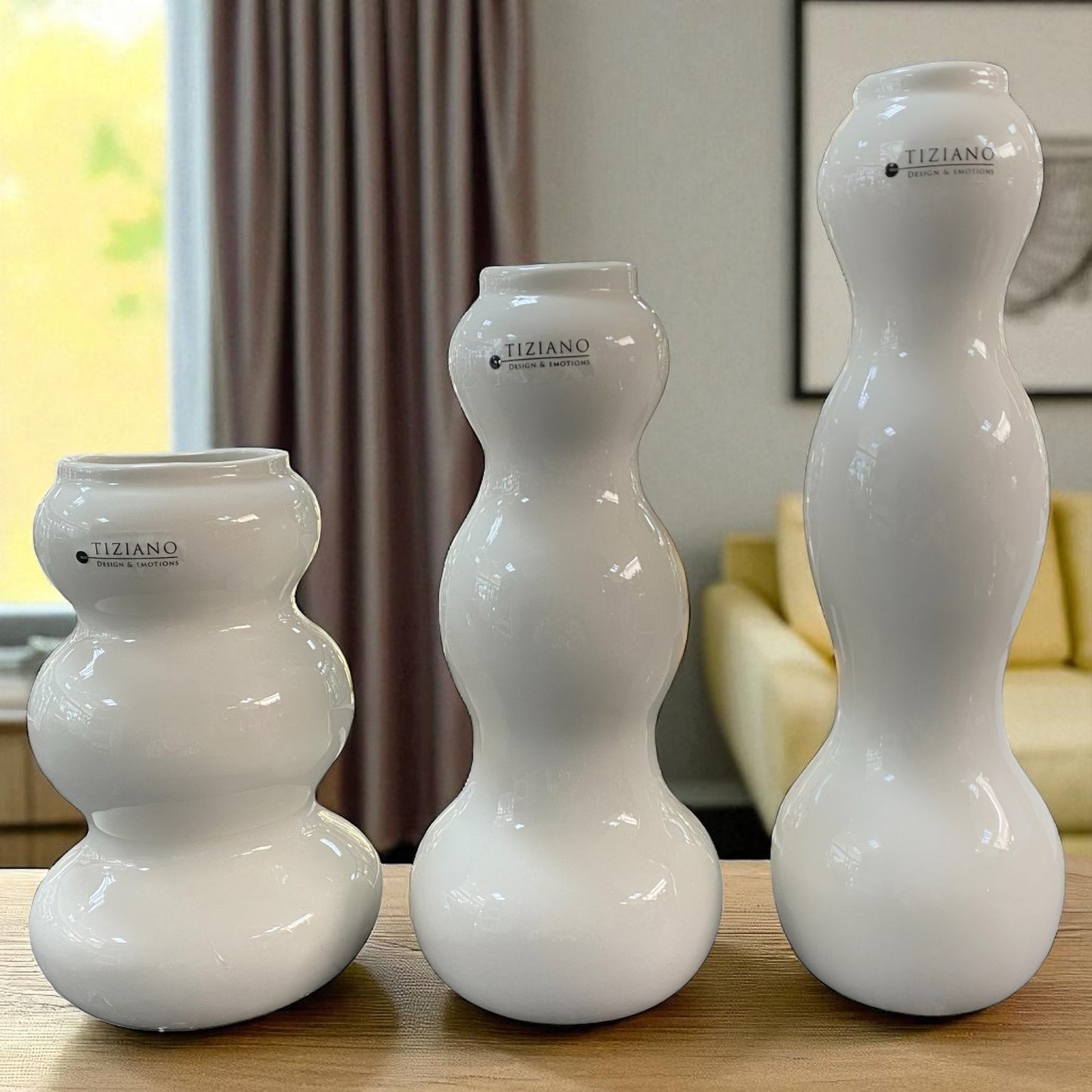Set von drei glänzenden creme-weißen Keramikvasen in geschwungener Form mit Tiziano Logo und in unterschiedlichen Höhen 16,5 cm, 21,5 cm und 26,5 cm im Ambiente