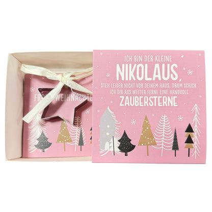 Offene Schachtel mit pinker Karte mit Aufschrift „Nikolaus“ und daran befestigter sternförmiger Ausstechform liegt vor weißem Hintergrund.